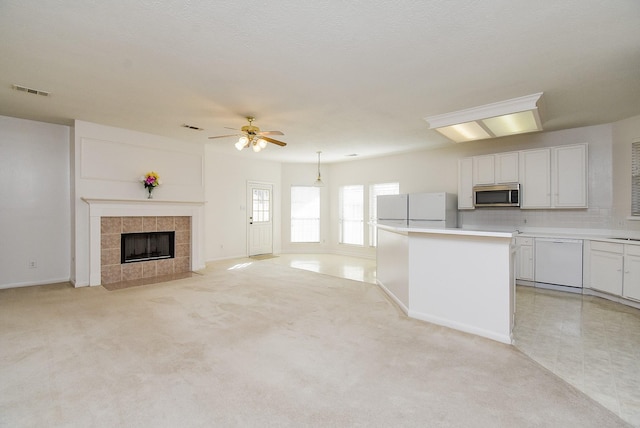 kitchen with white appliances, a center island, a fireplace, white cabinets, and light carpet