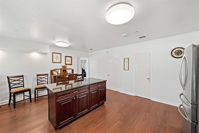 kitchen featuring dark brown cabinetry, dark hardwood / wood-style floors, stainless steel refrigerator, and a kitchen island