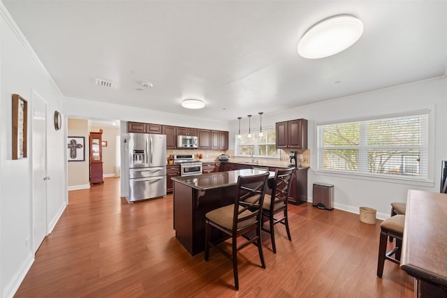 kitchen featuring a breakfast bar, decorative light fixtures, a kitchen island, stainless steel appliances, and hardwood / wood-style floors