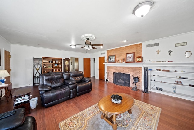 living room featuring a brick fireplace, wood-type flooring, ornamental molding, and ceiling fan