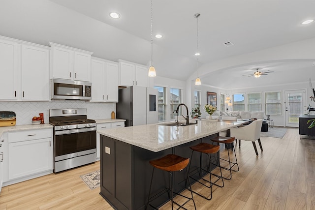 kitchen with stainless steel appliances, white cabinetry, hanging light fixtures, and a kitchen island with sink