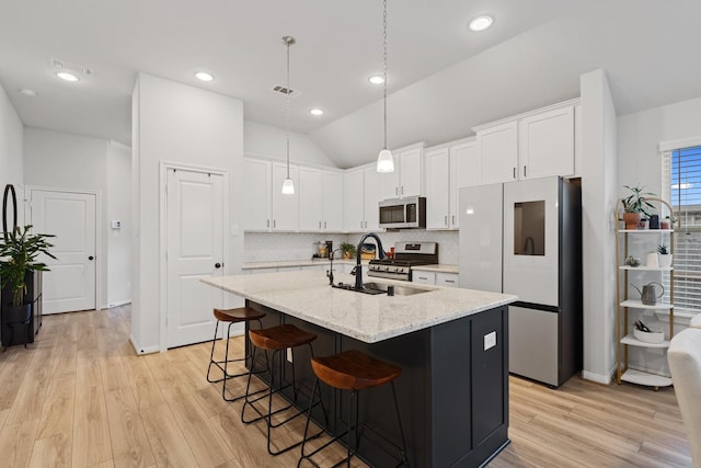 kitchen featuring sink, appliances with stainless steel finishes, light stone countertops, white cabinets, and a center island with sink