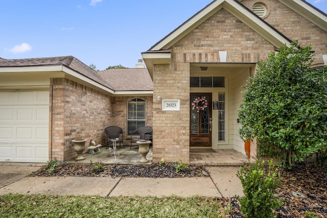 view of exterior entry featuring brick siding, roof with shingles, and an attached garage