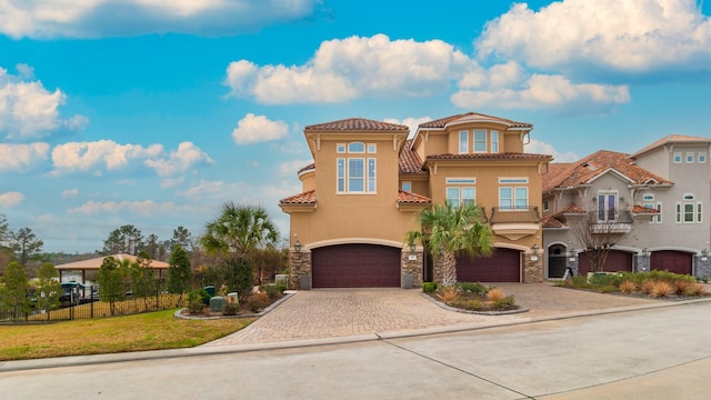 view of front of house featuring a garage, stone siding, fence, decorative driveway, and stucco siding