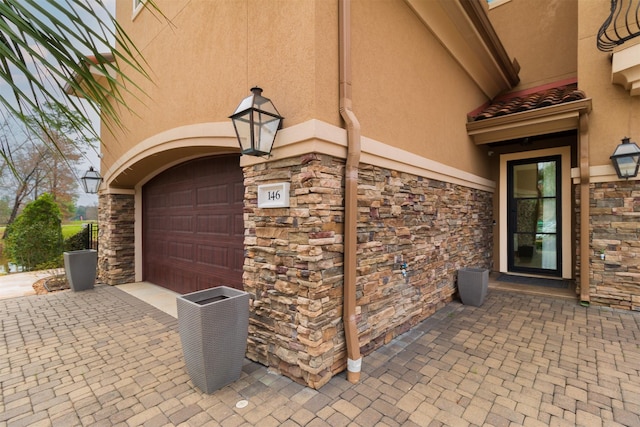 view of exterior entry featuring a garage, stone siding, and stucco siding