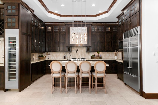 kitchen with an island with sink, built in refrigerator, a raised ceiling, and decorative backsplash