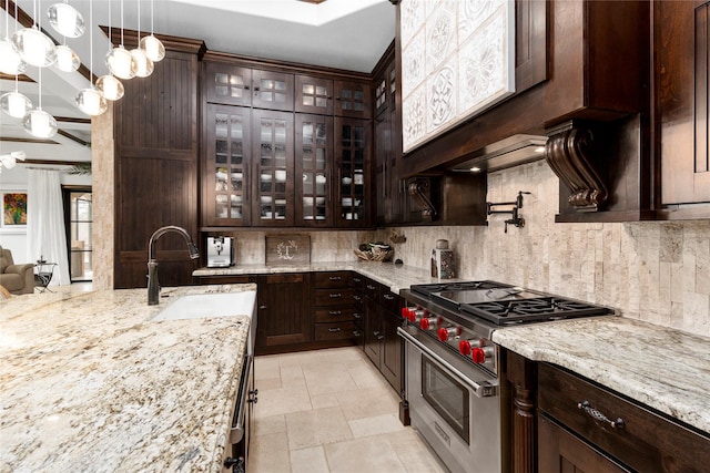 kitchen with luxury stove, stone tile flooring, dark brown cabinets, decorative backsplash, and decorative light fixtures