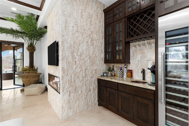 bar with indoor wet bar, stone tile floors, a glass covered fireplace, a sink, and beverage cooler