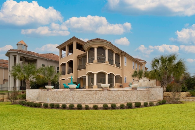 back of property with a balcony, stucco siding, fence, and a yard