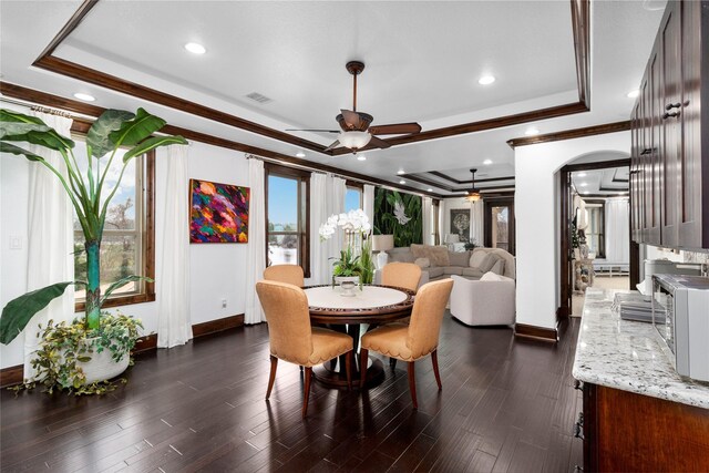 dining room with dark wood-style floors, a raised ceiling, and crown molding