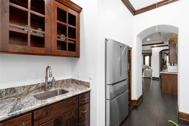 kitchen featuring arched walkways, dark wood-style flooring, freestanding refrigerator, crown molding, and a sink