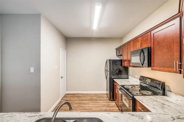 kitchen featuring light stone countertops, sink, light wood-type flooring, and black appliances