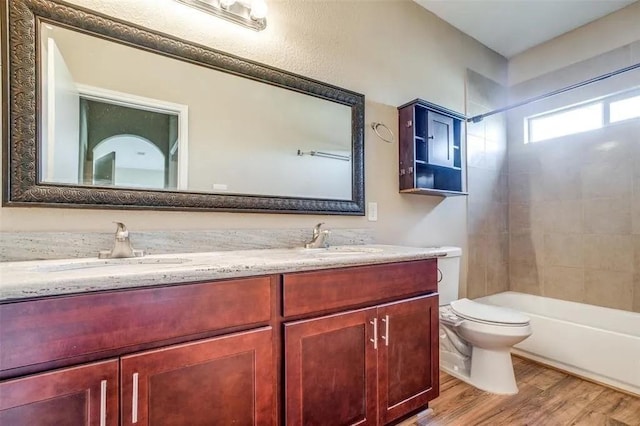 full bathroom featuring hardwood / wood-style flooring, vanity, tiled shower / bath combo, and toilet