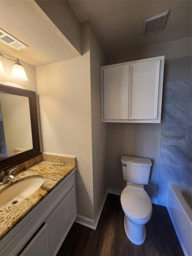 bathroom featuring hardwood / wood-style flooring, a tub to relax in, vanity, and toilet