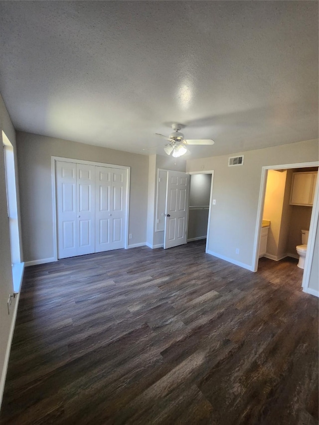 unfurnished bedroom with ceiling fan, dark hardwood / wood-style floors, two closets, and a textured ceiling