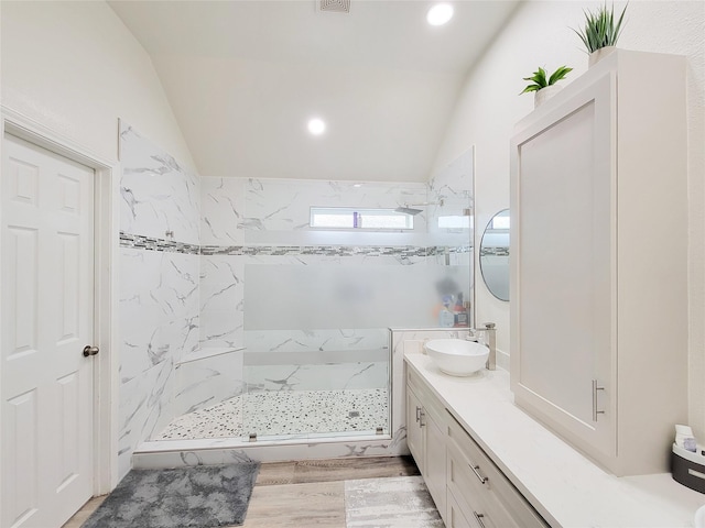 bathroom with hardwood / wood-style floors, tiled shower, vaulted ceiling, and vanity