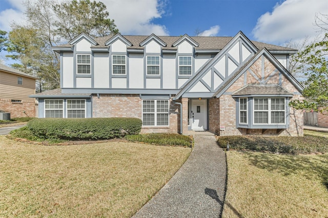 english style home with stucco siding, a front yard, roof with shingles, and brick siding