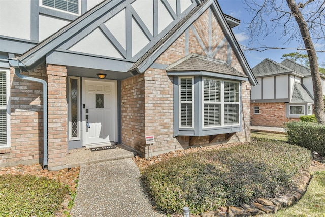 property entrance with roof with shingles, stucco siding, and brick siding