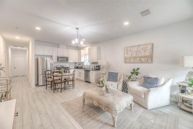 living area featuring visible vents, light wood-style floors, recessed lighting, and an inviting chandelier