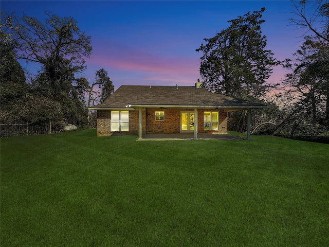 back house at dusk featuring a patio area and a lawn