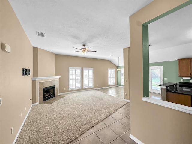 unfurnished living room featuring vaulted ceiling, a textured ceiling, light tile patterned floors, ceiling fan, and a tiled fireplace