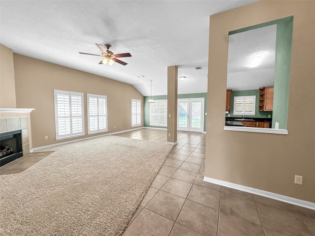 unfurnished living room featuring lofted ceiling, light colored carpet, a textured ceiling, a tile fireplace, and ceiling fan