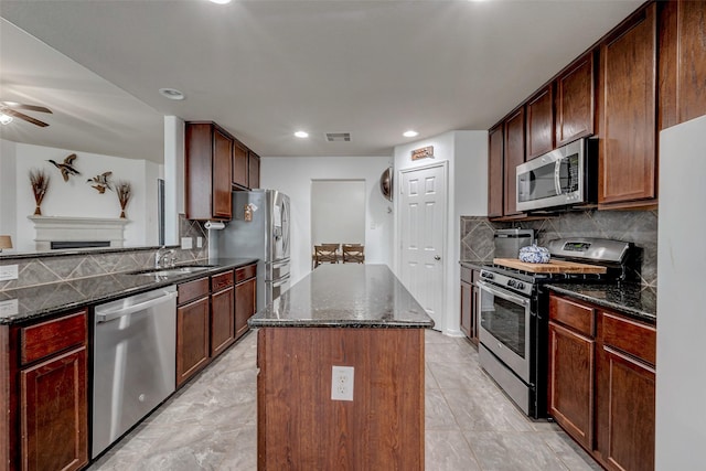 kitchen with a kitchen island, a sink, appliances with stainless steel finishes, decorative backsplash, and dark stone counters