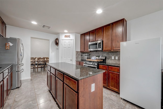 kitchen with visible vents, appliances with stainless steel finishes, dark stone countertops, a center island, and backsplash