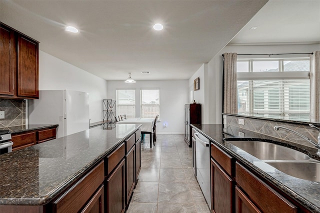 kitchen featuring backsplash, stainless steel dishwasher, freestanding refrigerator, a kitchen island, and a sink