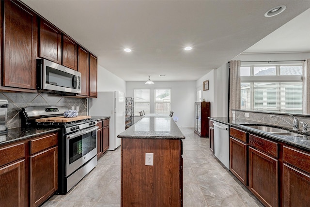 kitchen featuring dark stone counters, stainless steel appliances, a sink, and a center island