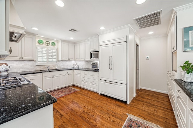 kitchen featuring visible vents, a sink, premium range hood, built in appliances, and dark wood-style flooring