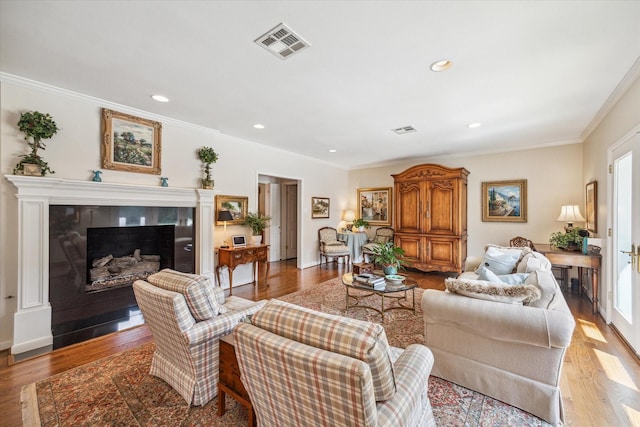 living room with visible vents, light wood-style flooring, recessed lighting, ornamental molding, and a tiled fireplace