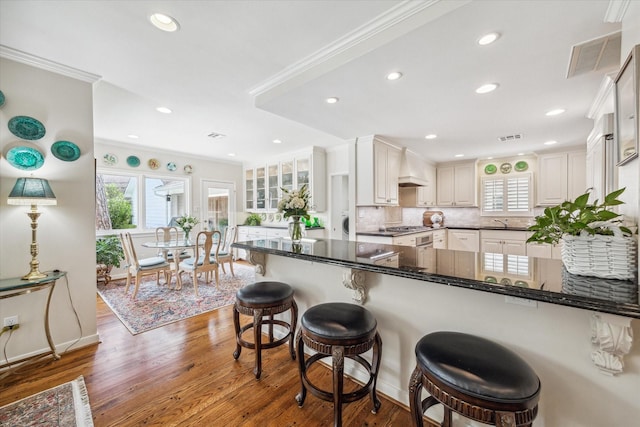 kitchen with custom exhaust hood, crown molding, visible vents, and a healthy amount of sunlight