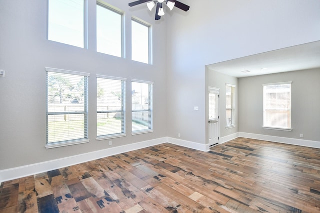 unfurnished living room featuring hardwood / wood-style flooring, a towering ceiling, and ceiling fan