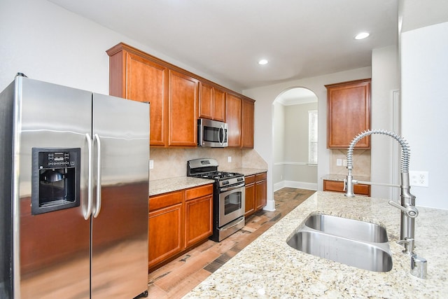 kitchen featuring tasteful backsplash, light stone countertops, appliances with stainless steel finishes, and sink