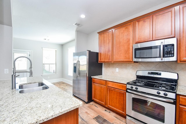 kitchen featuring appliances with stainless steel finishes, sink, backsplash, light stone counters, and light hardwood / wood-style flooring