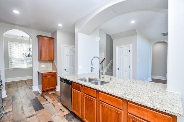 kitchen with sink, stainless steel dishwasher, a kitchen island with sink, light stone countertops, and light hardwood / wood-style floors