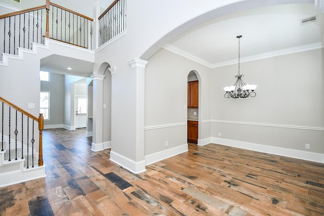 interior space with decorative columns, wood-type flooring, a chandelier, a high ceiling, and crown molding