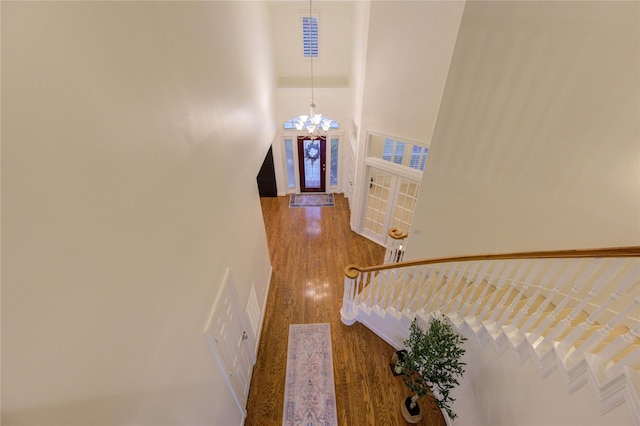 hallway with a notable chandelier, a towering ceiling, and wood finished floors