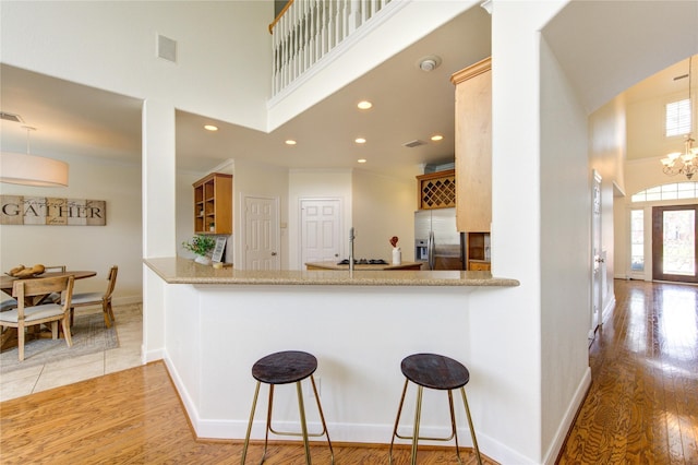 kitchen with light wood-style flooring, a notable chandelier, a high ceiling, baseboards, and stainless steel refrigerator with ice dispenser