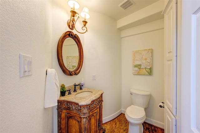 half bathroom with visible vents, toilet, vanity, wood finished floors, and baseboards