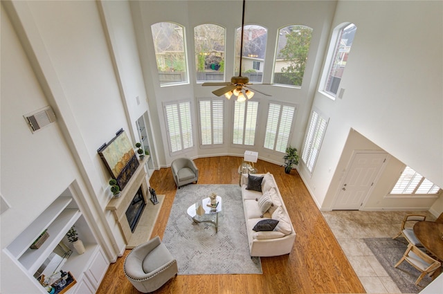 living room featuring a fireplace, visible vents, a towering ceiling, wood finished floors, and baseboards