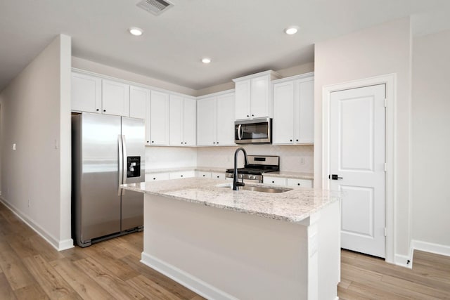 kitchen featuring a kitchen island with sink, white cabinetry, stainless steel appliances, light stone countertops, and light wood-type flooring