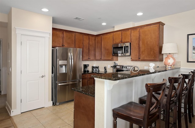 kitchen with a breakfast bar area, tasteful backsplash, dark stone countertops, kitchen peninsula, and stainless steel appliances