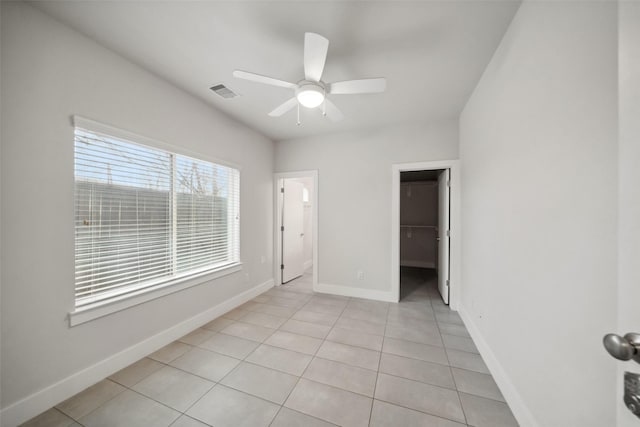 unfurnished bedroom featuring light tile patterned flooring, a spacious closet, ceiling fan, and a closet