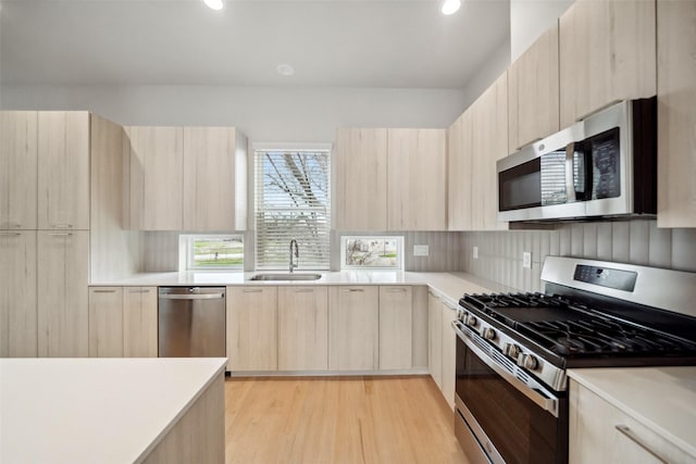 kitchen with sink, appliances with stainless steel finishes, light brown cabinetry, decorative backsplash, and light wood-type flooring