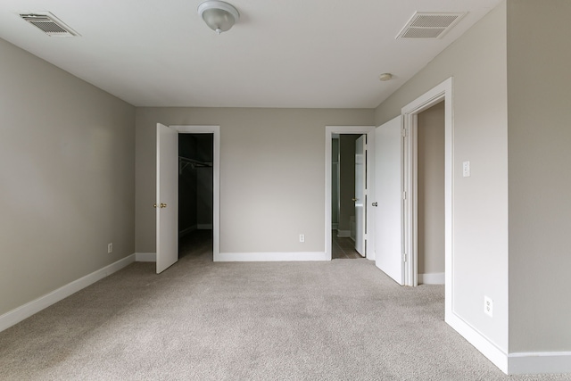 unfurnished bedroom featuring light carpet, a walk in closet, a closet, and ensuite bathroom