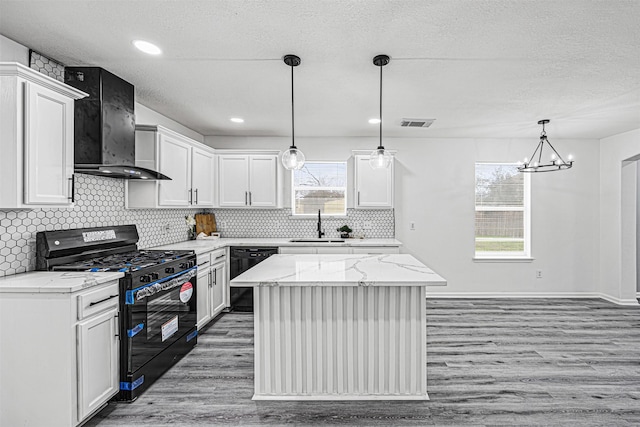 kitchen featuring a center island, hanging light fixtures, white cabinetry, wall chimney range hood, and black appliances