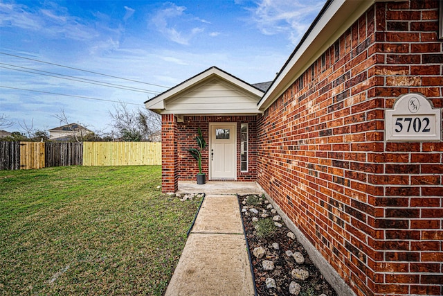 entrance to property featuring a yard, brick siding, and fence