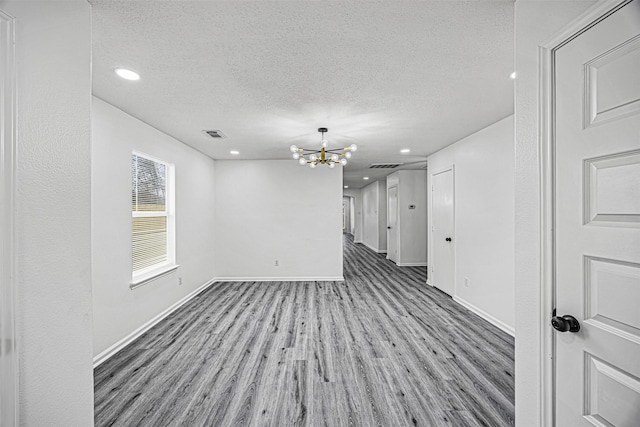 unfurnished room featuring visible vents, light wood-style flooring, an inviting chandelier, a textured ceiling, and baseboards